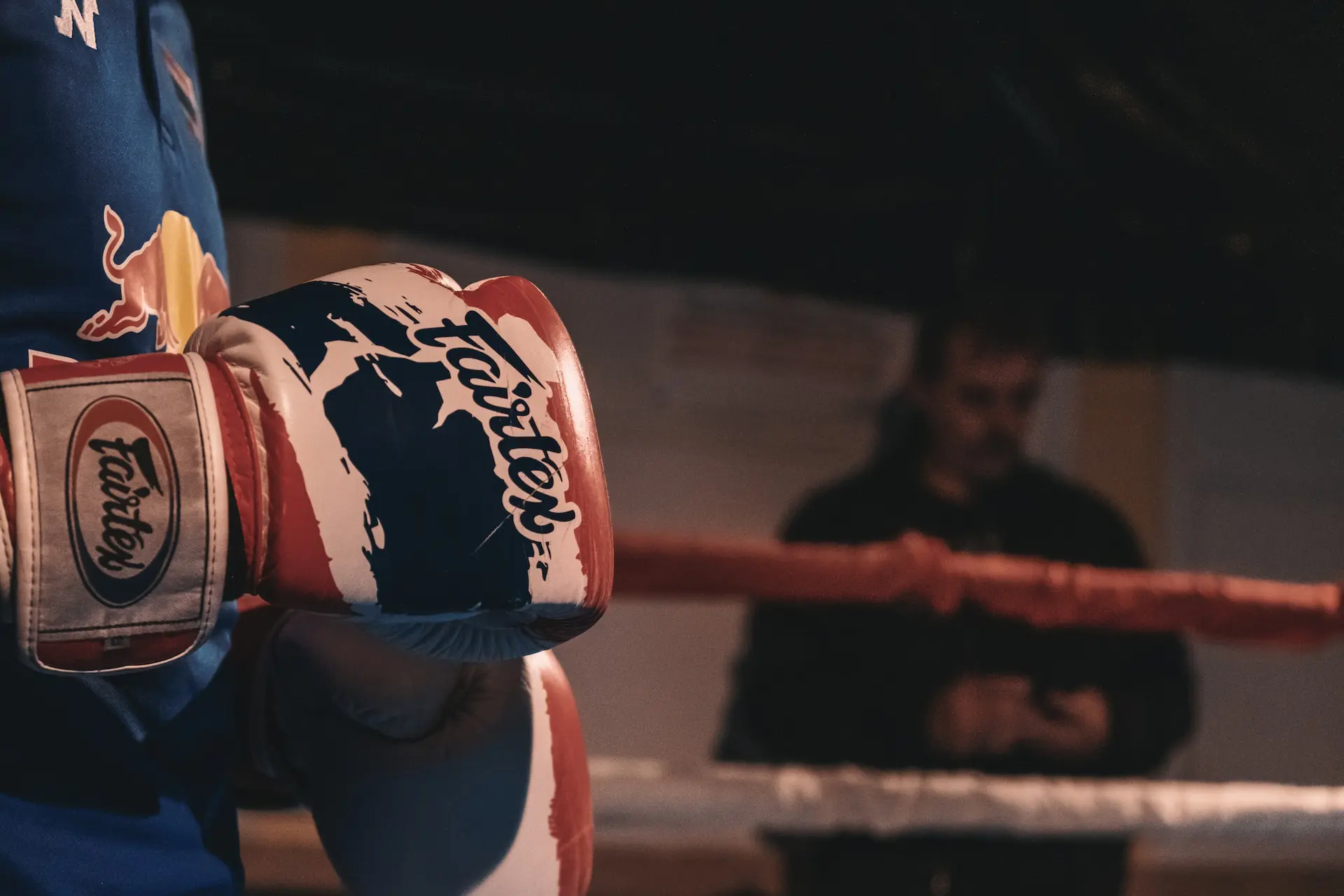 gant de boxe rouge et bleu avec logo, ring de combat en arrière-plan flou