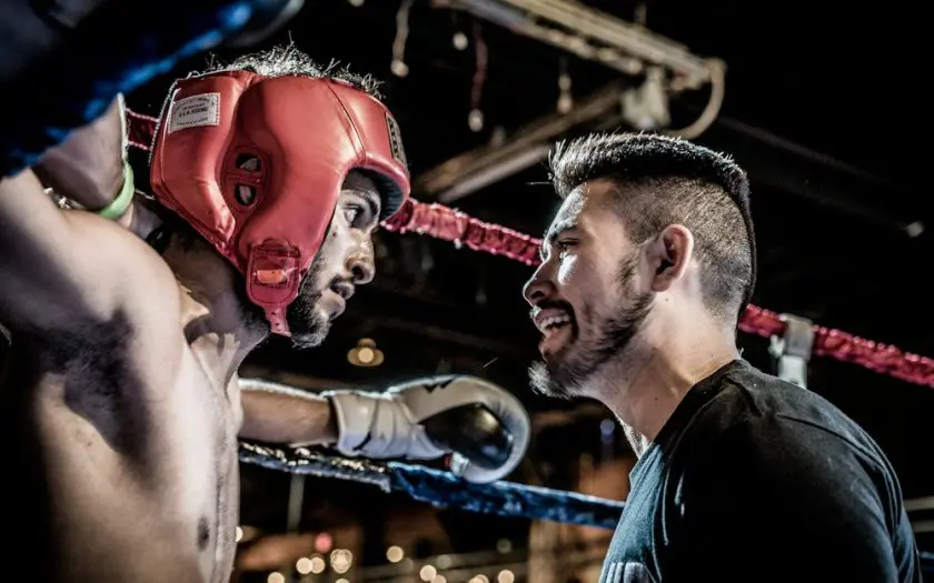 deux combattants de MMA face à face dans un ring, l'un portant un casque de protection rouge