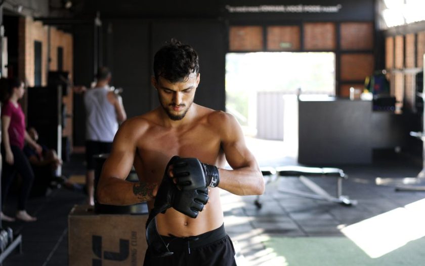 Shirtless man preparing for an intense workout session in a gym, wearing boxing gloves.