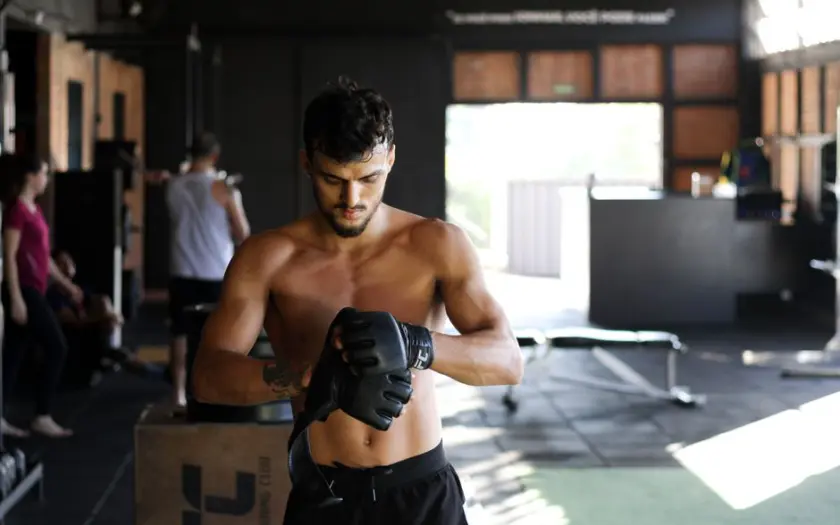 Shirtless man preparing for an intense workout session in a gym, wearing boxing gloves.