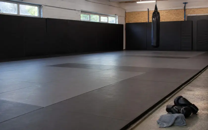 salle d'entraînement vide avec tapis de sol gris, sacs de boxe et équipements de MMA
