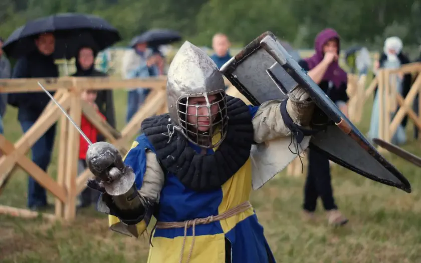 A knight in full armor engaged in a lively medieval reenactment outdoors.