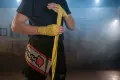 A close-up of an MMA fighter wrapping his hands with yellow bandages in a smoky gym setting.