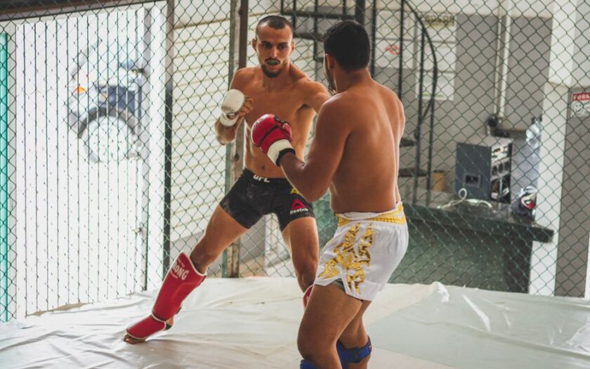 Two men engage in intense kickboxing sparring inside a gym arena.
